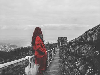 Rear view of woman standing by railing against sky