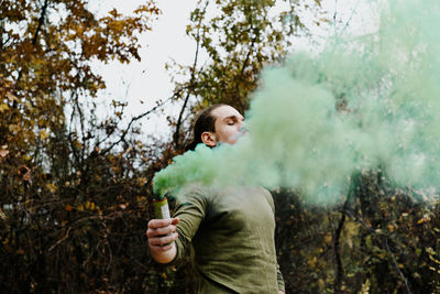 Young man holding distress flare while standing in forest