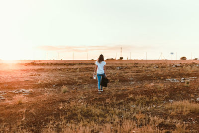 Rear view of woman walking on field against clear sky