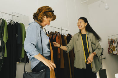 Smiling sales staff assisting senior female customer while choosing dress at store