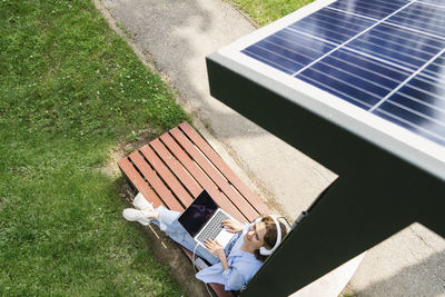 Smiling woman sitting under solar charging point at park