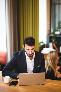 Confident male entrepreneur using laptop while sitting at table in office