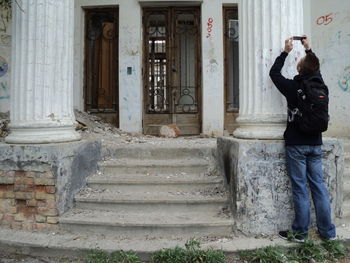 Full length of man photographing column through mobile phone while standing at entrance of building