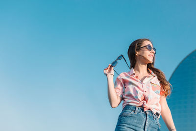 Young woman wearing sunglasses standing against blue sky