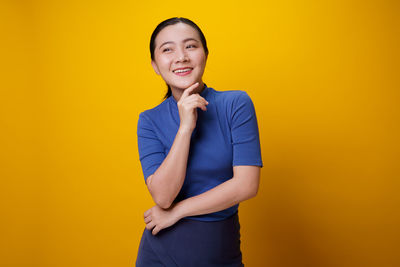 Portrait of smiling young woman against yellow background