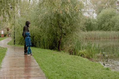 A man with a child in a jacket with a hood, stand and look at the lake on a rainy day