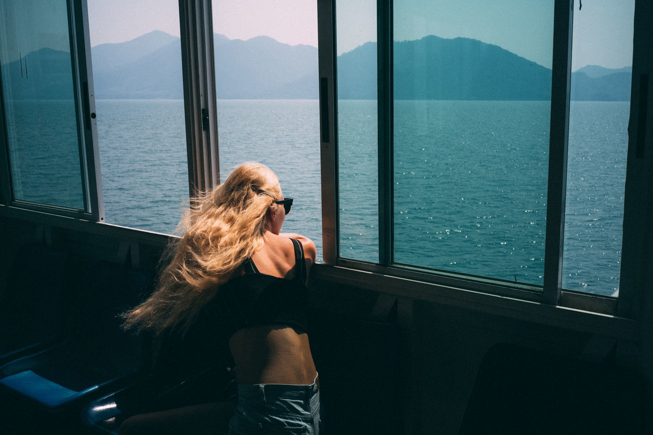 real people, window, one person, sea, lifestyles, water, leisure activity, nature, transparent, mountain, women, hair, sitting, mode of transportation, transportation, glass - material, long hair, day, hairstyle, outdoors