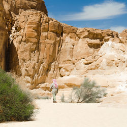 Rear view of woman walking on rock formation against sky