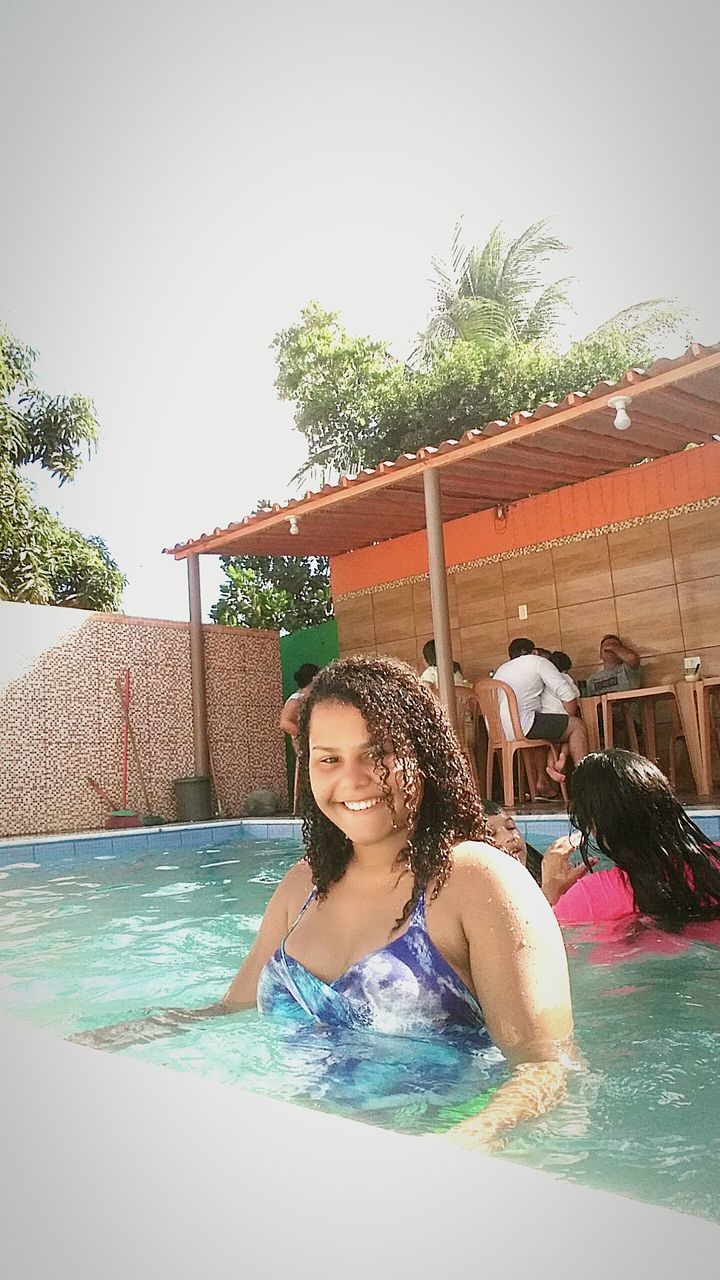 HAPPY YOUNG WOMAN IN SWIMMING POOL AGAINST TREE