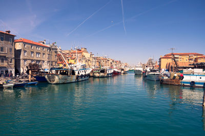 Sailboats moored on harbor in city against clear blue sky