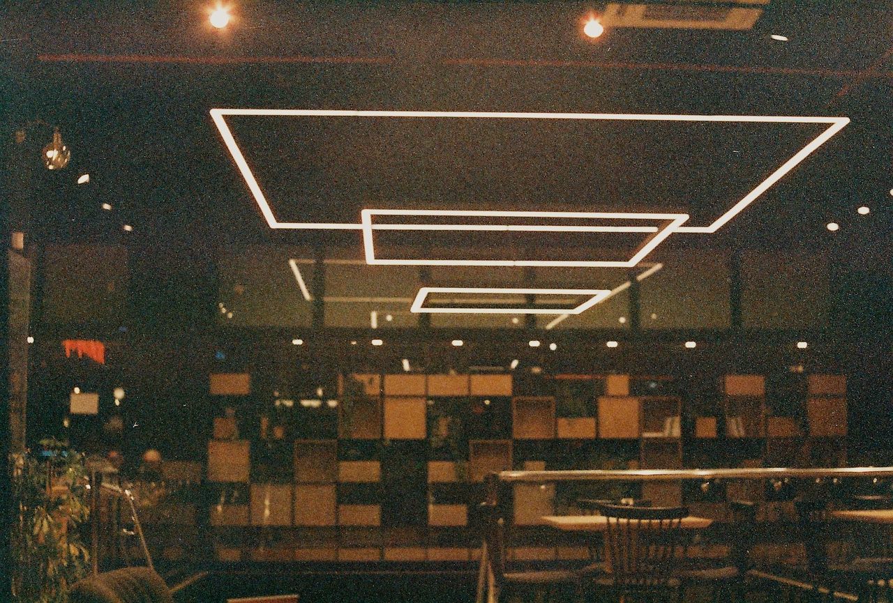 night, illuminated, architecture, built structure, lighting equipment, no people, city, absence, indoors, railing, table, cafe, seat, empty, transparent, building, chair, electric lamp