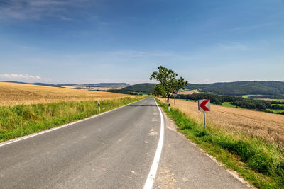 Empty road amidst field against sky