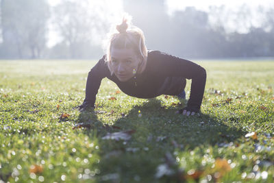 Confident woman doing push-ups on grassy field at park during sunny day