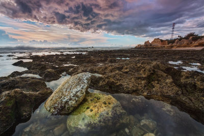 Rocks on beach against sky during sunset