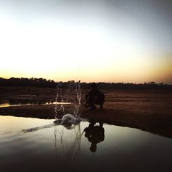 Silhouette man on shore against sky during sunset