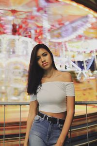 Portrait of young woman standing illuminated amusement park ride at night