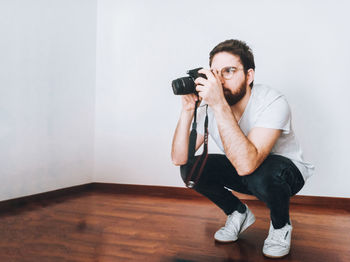 Young man photographing against wall at home