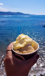 Cropped image of person holding ice cream in sea