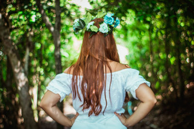 Rear view of woman standing against trees in forest