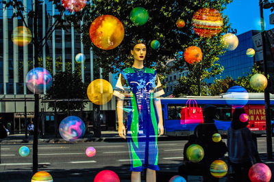 Mannequin and colorful decorations at store seen through glass