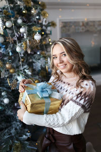 Happy cute girl in a cozy sweater celebrates christmas prepares gift boxes at home indoor