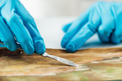 Professional painting conservator uses scalpel to carefully remove patches from an oil painting