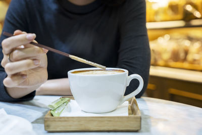 Midsection of woman stirring cappuccino at table