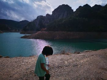Rear view of boy looking at lake against mountain