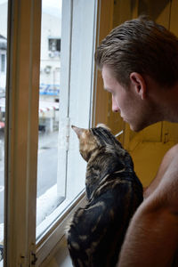 Man and cat looking through window