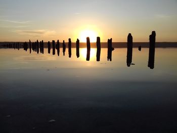 Silhouette wooden posts in sea against sky during sunset