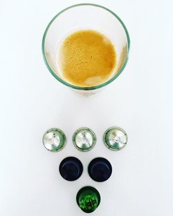 Directly above shot of coffee capsules and drinking glass against white background