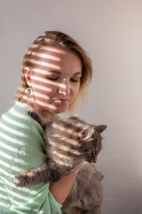 Portrait of young woman with cat against white background