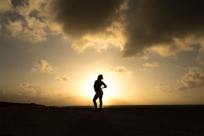 Silhouette woman standing at beach against sky during sunset