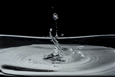 Close-up of drop splashing on water against black background