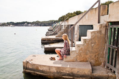 Side view of woman sitting on steps by sea