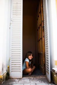 Full length of girl sitting at entrance of house