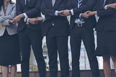 Midsection of business people holding hands standing outdoors