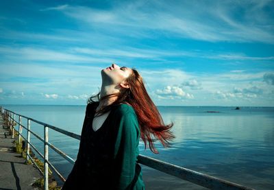 Side view of a woman relaxing on railing by calm sea