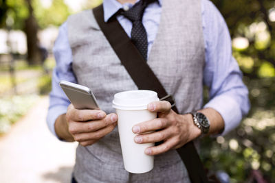 Close-up of businessman with coffee and smartphone in city park
