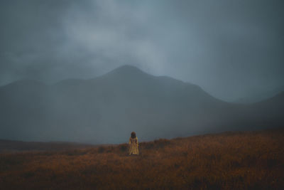 Rear view of woman standing on field against mountain during foggy weather