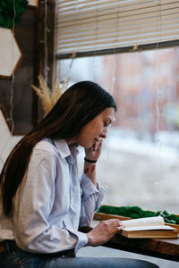 Brunette girl by the window in a cafe drinking coffee, reading a book