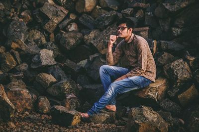 Thoughtful young man looking away while sitting on rock