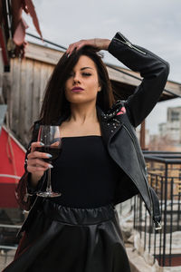 Low angle portrait of woman holding red wine against sky