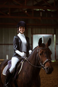 Portrait of smiling woman riding horse in stable