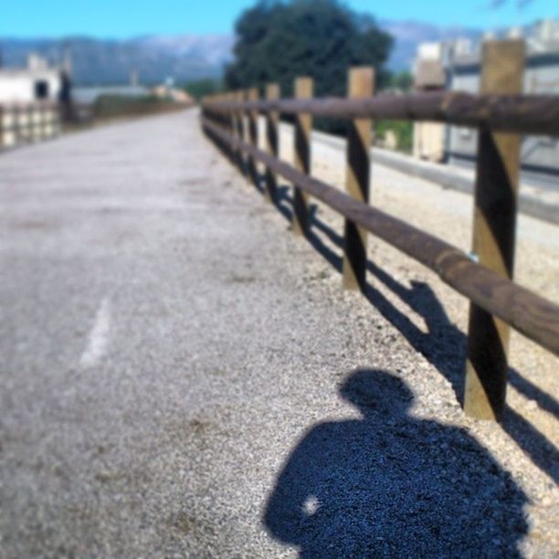 shadow, focus on foreground, selective focus, sunlight, surface level, street, incidental people, outdoors, railing, day, road, close-up, built structure, bench, sunny, walking, sidewalk, nature, sand