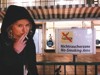 Young woman smoking in front of no smoking sign