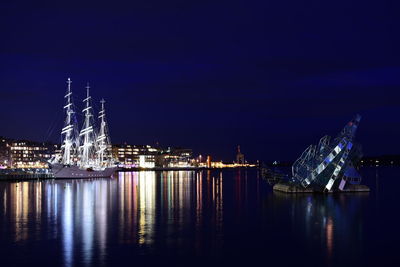 Illuminated city by sea against sky at night