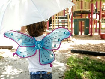 Rear view of girl with umbrella walking on field at park