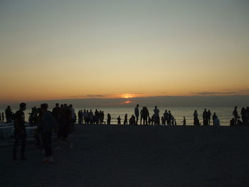 Silhouette people on beach against sky during sunset