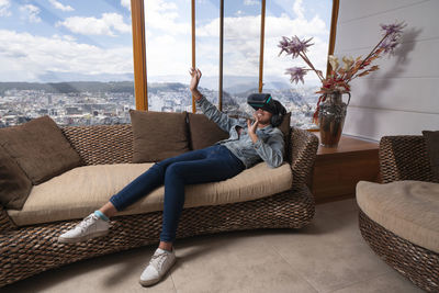 Woman sitting on sofa at home using virtual reality glasses